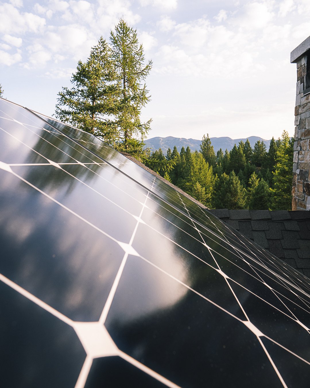Solar panels on a Montana roof with evergreen forest and mountain ridgelines beyond